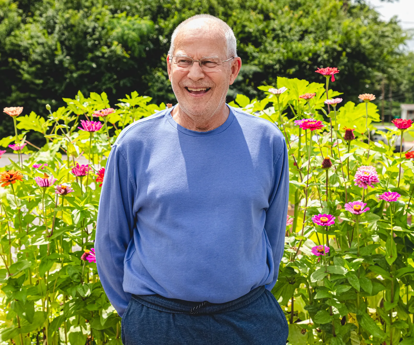 A smiling older adult standing among blooming flowers at The Legacy Center